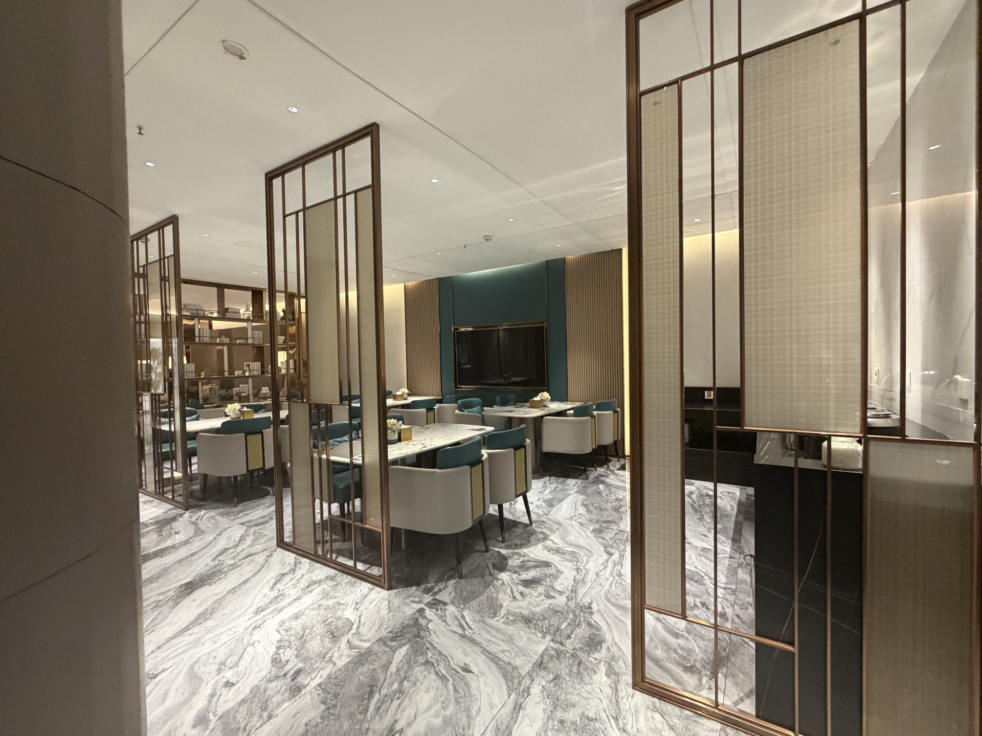 Refined VIP lounge with brass-framed screens, teal accent chairs and marble flooring